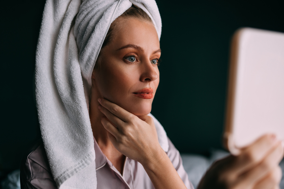 Woman looks at glowing, healthy skin in mirror after a series of Hydrafacial treatments for acne